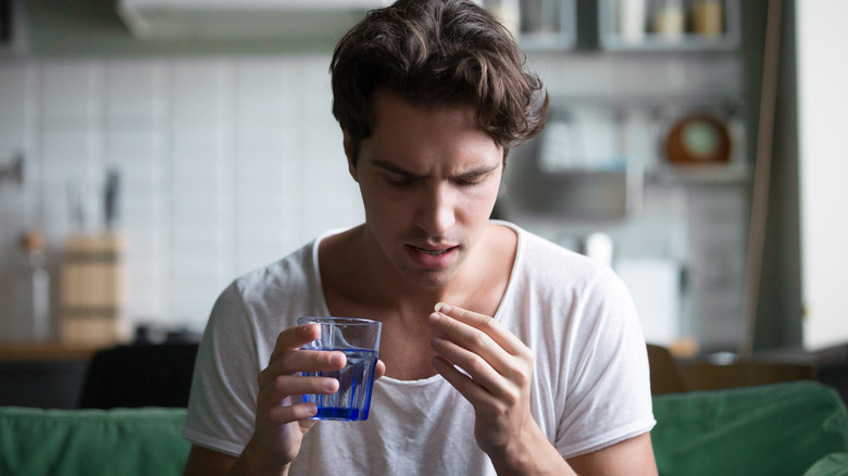 Man holding glass of water and a pill 