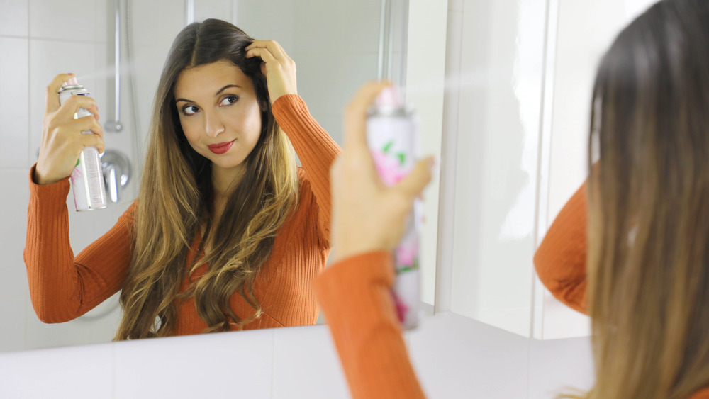 Woman using dry shampoo while looking in the mirror