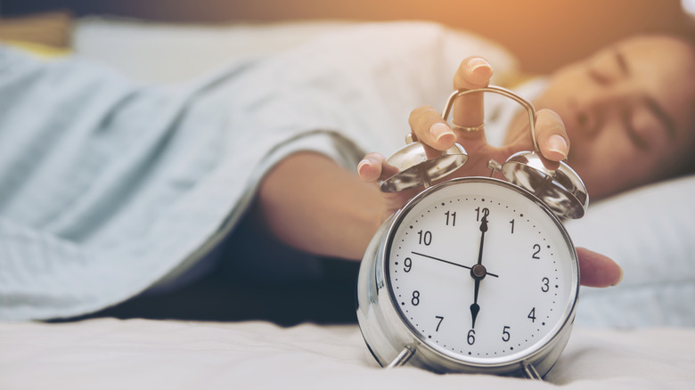 woman laying in bed hitting snooze button