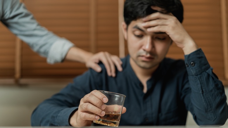 Troubled man holding glass of alcohol