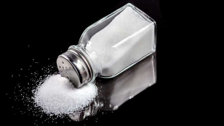 Close up of a salt shaker on its side with salt spilled out on a black surface