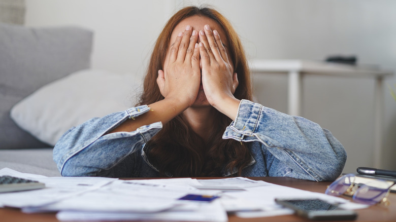 Woman covering her face with her hands as she sits at a table covered with paperwork