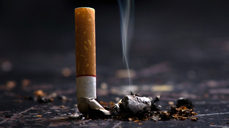Close up of a cigarette partially crushed but still smoking against a dark surface