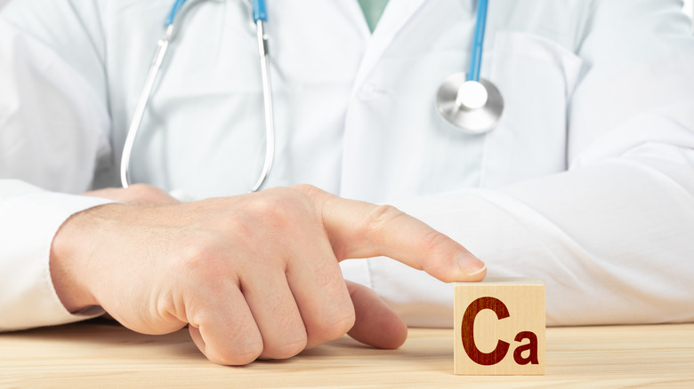 Close up of a doctor in a white coat pointing to a wooden block with the symbol for calcium
