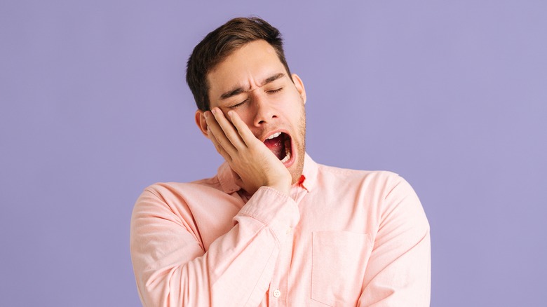 Man yawning against a violet background