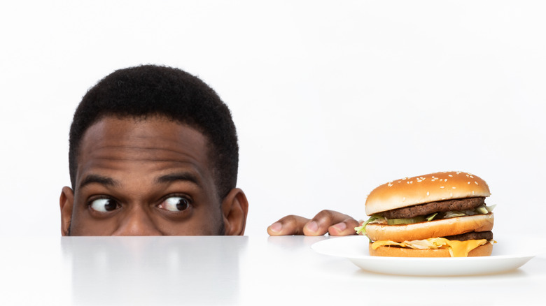 Man peeking wide eyed at a burger