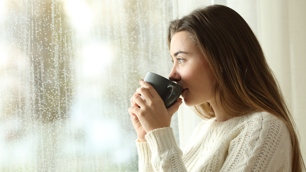 woman drinking coffee looking outside window