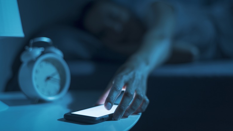 Hand reaching for phone beside bed