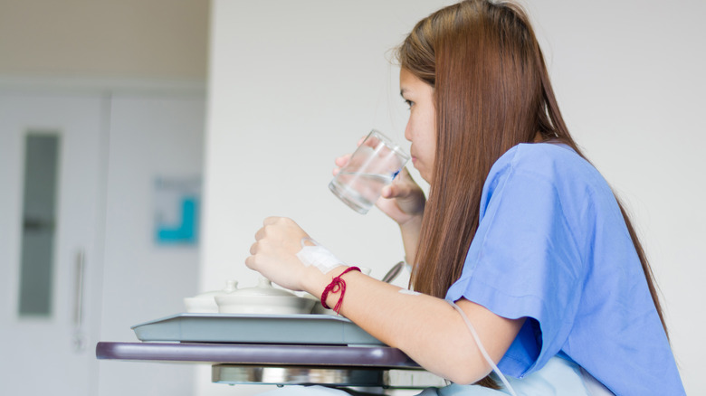 a person sits up in hospital bed to drink and eat