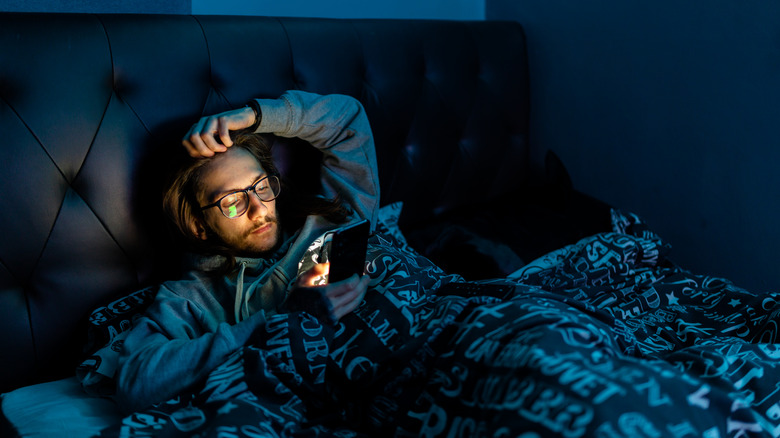 man checking phone in bed