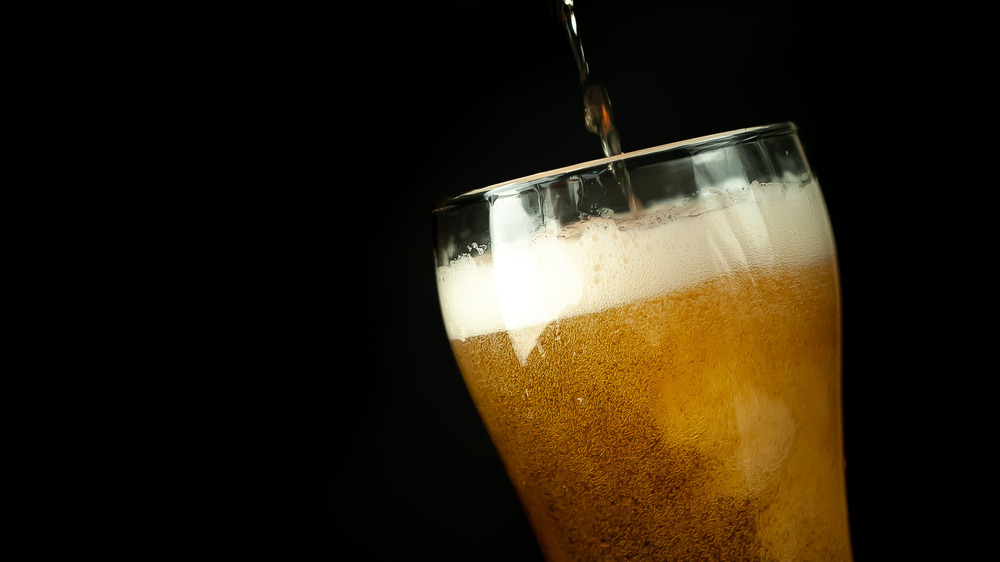 A glass of beer being poured against a black background