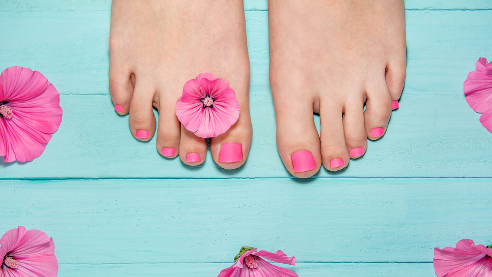 Close up of pedicured feet next to flowers against a blue background