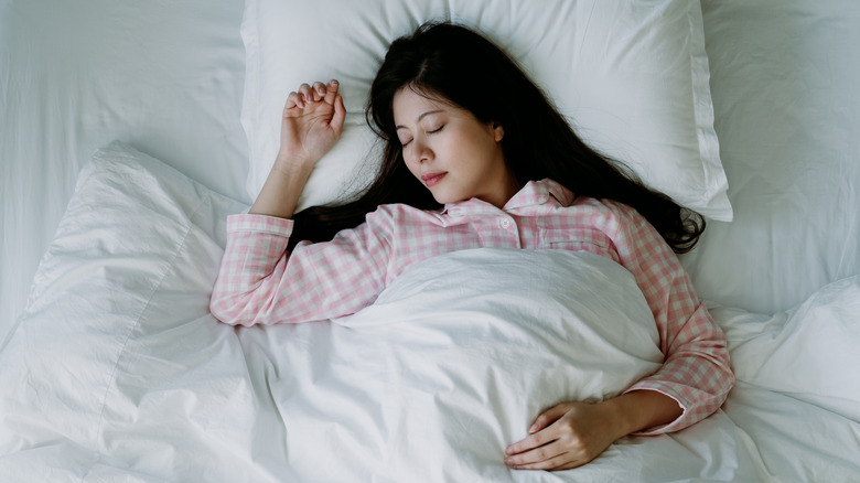 a woman in pink pajamas sleeps face up on white sheets