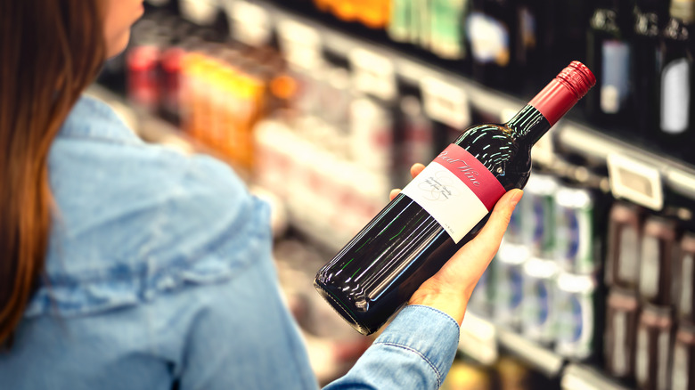 woman contemplating a wine bottle in front of shelves of alcohol