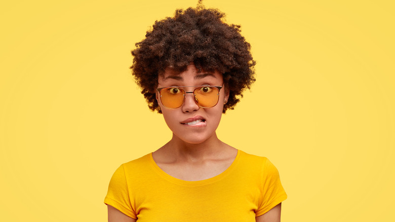 Woman in glasses and a yellow shirt biting her lip in embarrassment