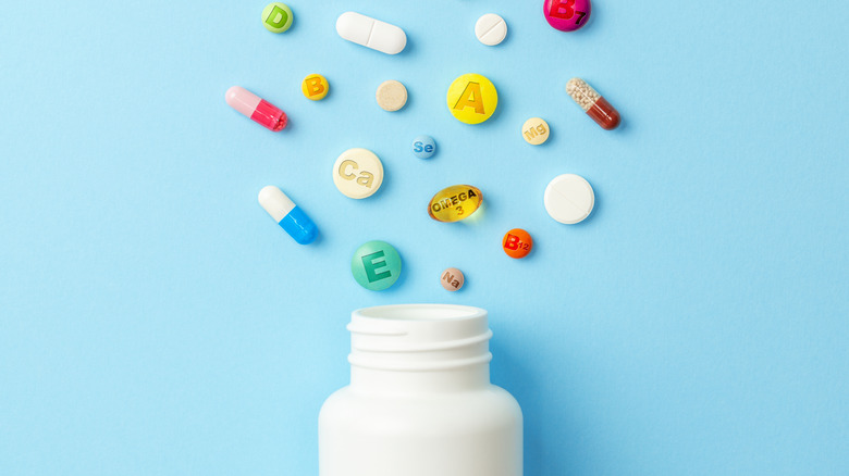 A variety of different vitamin supplements popping out of a white vitamin bottle