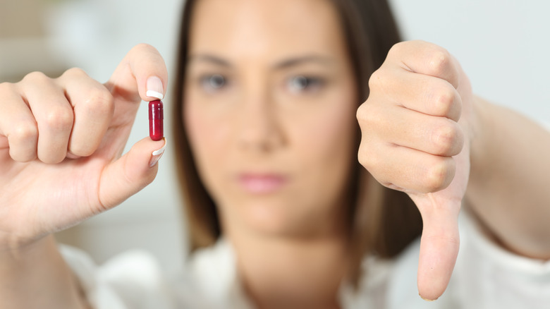 A woman holding up a red pill in one hand and giving the thumbs down with her other hand