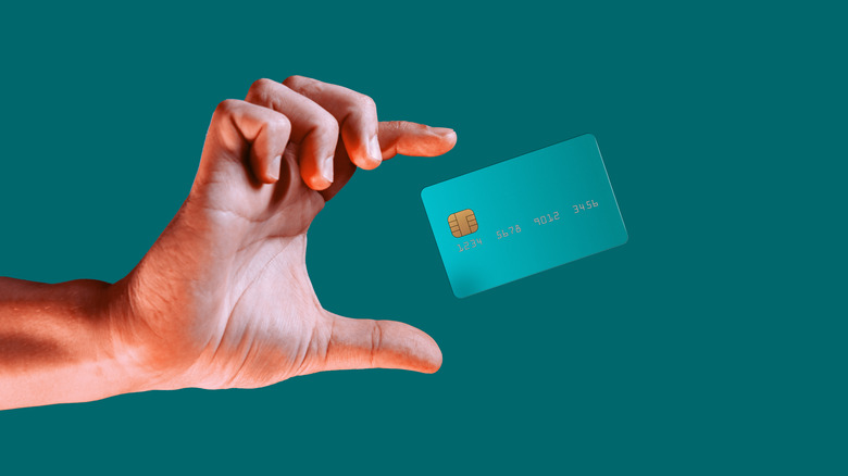 A hand attempting to grab a teal credit card in mid air