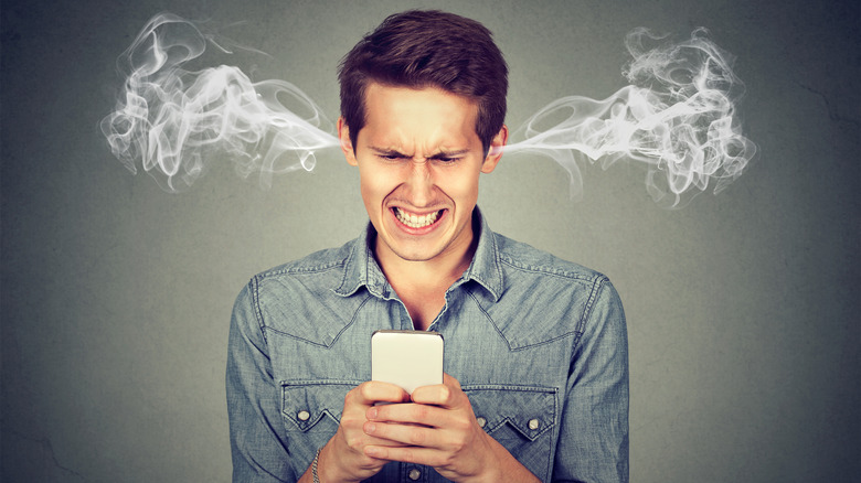 An angry man with smoke coming out of his ears glaring at his cellphone