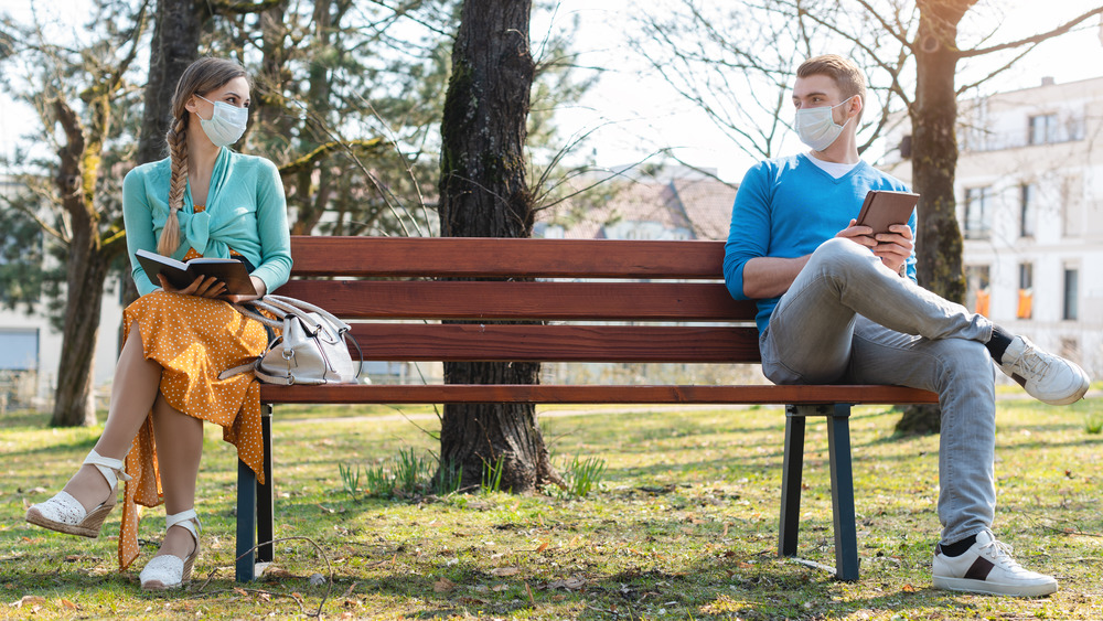 masked couple sitting on opposite ends of a bench