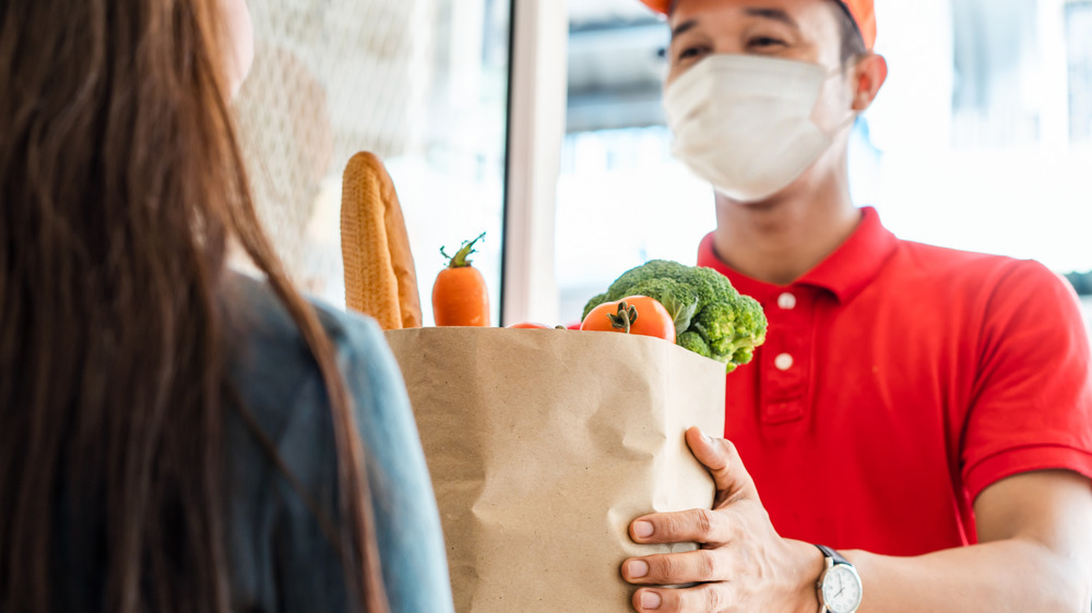 man in mask delivering bag of groceries to a woman