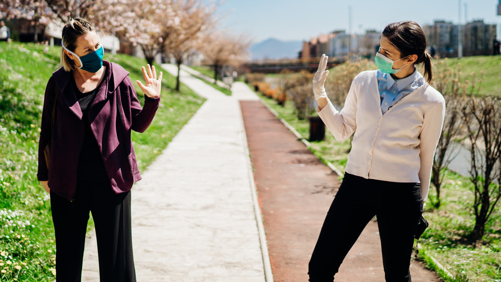 Two female friends in masks waving to each other outside