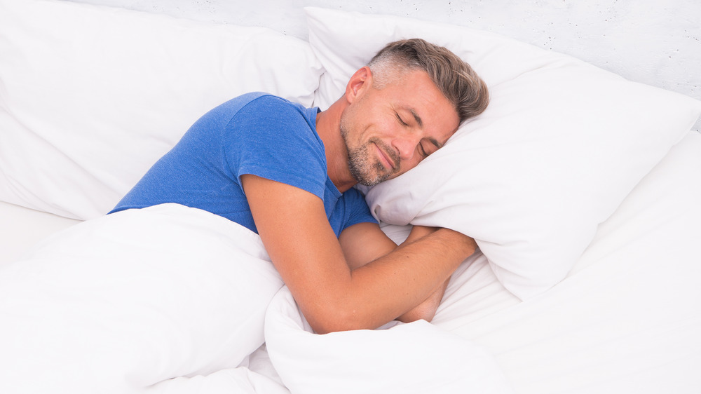 white man in blue t-shirt sleeping on white linens