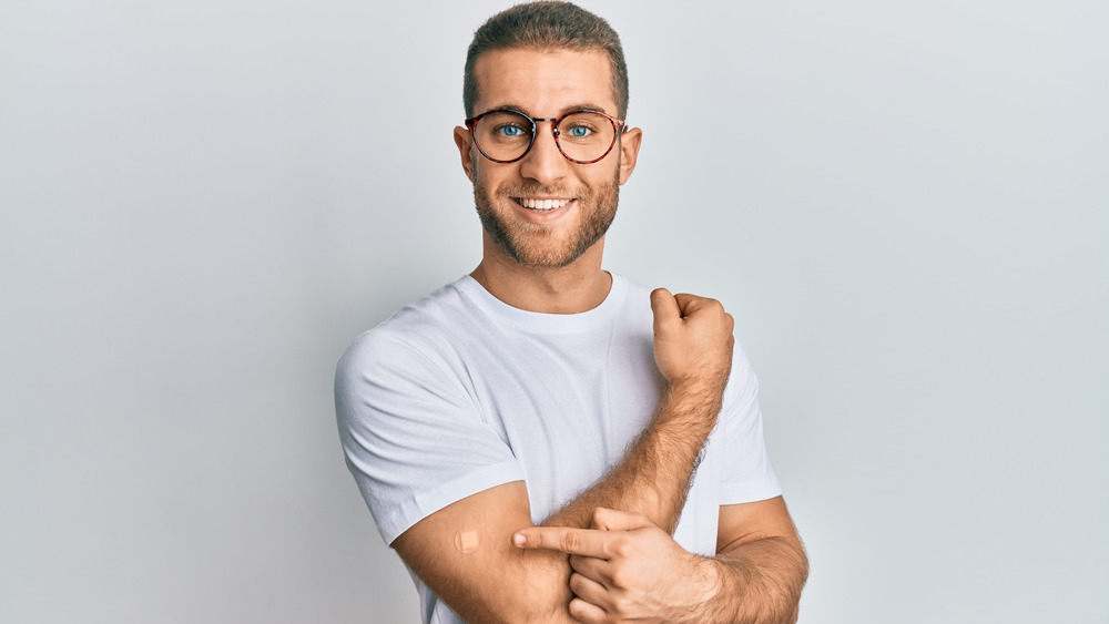 smiling white man pointing to bandaid on his arm