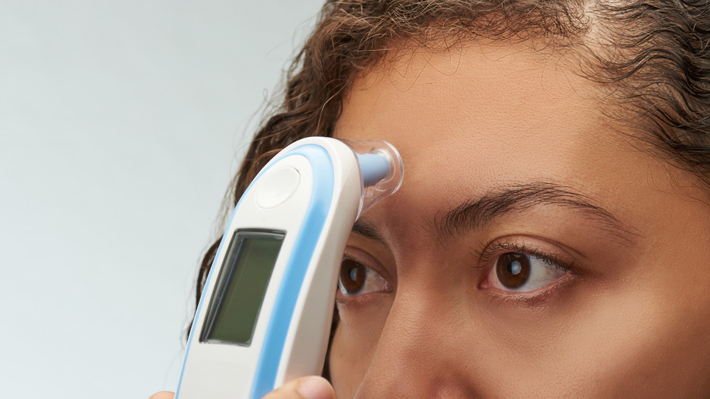 woman taking her own temperature with forehead thermometer