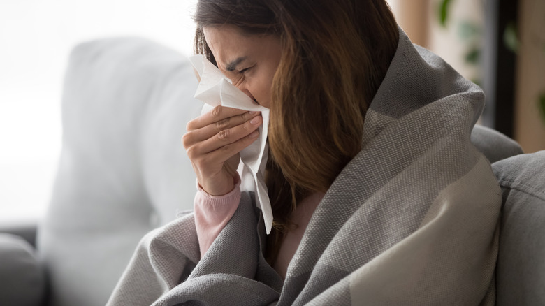 sick woman blowing nose into napkin