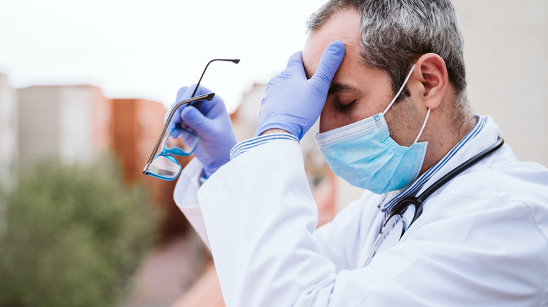 a doctor looking frazzled removing glasses and holding forehead