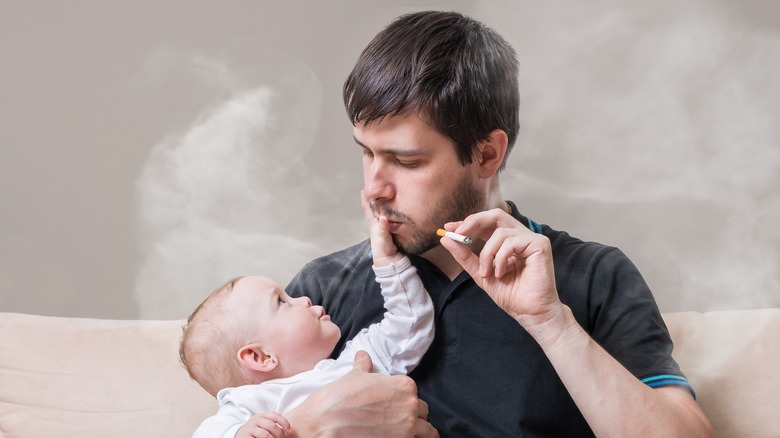 Man smoking while holding a newborn