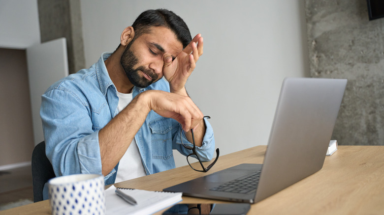 stressed man working and rubbing eyes