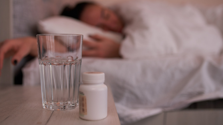 Woman in bed with bottle of sleeping pills on nightstand