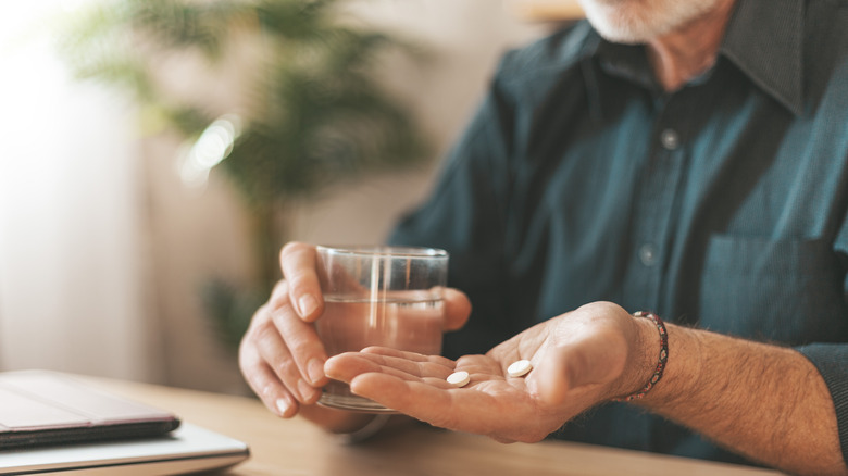 Hand holding medication and water glass