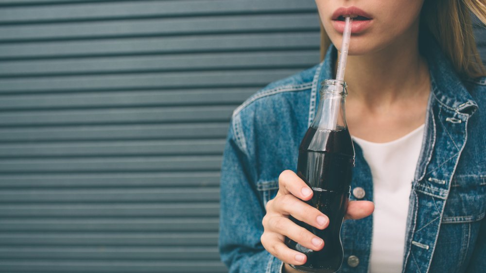 Close up of woman drinking soda from bottle with straw