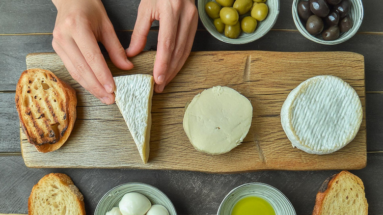 woman's hand putting cheese on wooden board