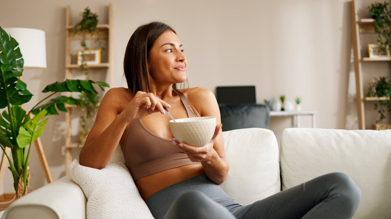 woman eating snack out of bowl while sitting on couch