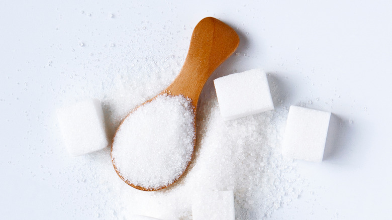 Sugar cubes and a wooden spoon full of sugar on a white background