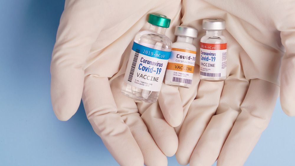 Two gloved hands holding three vials of COVID-19 vaccine