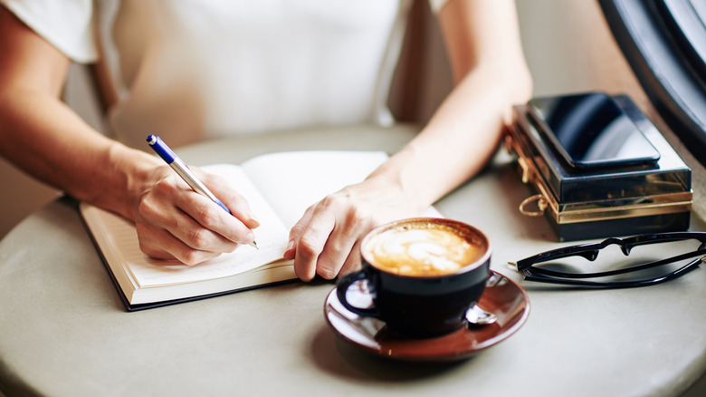 Hand writing in journal near coffee