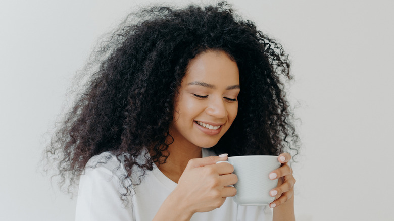 Woman smiling and looking at white mug of coffee