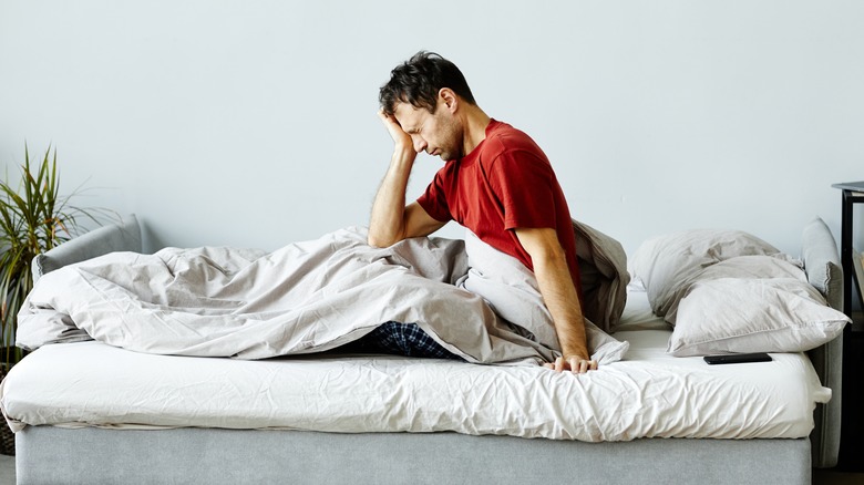 man sitting up in bed with his hand on his face