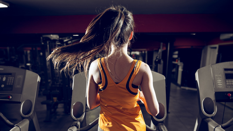 Rear view of woman with a ponytail running on the treadmill in the gym at night