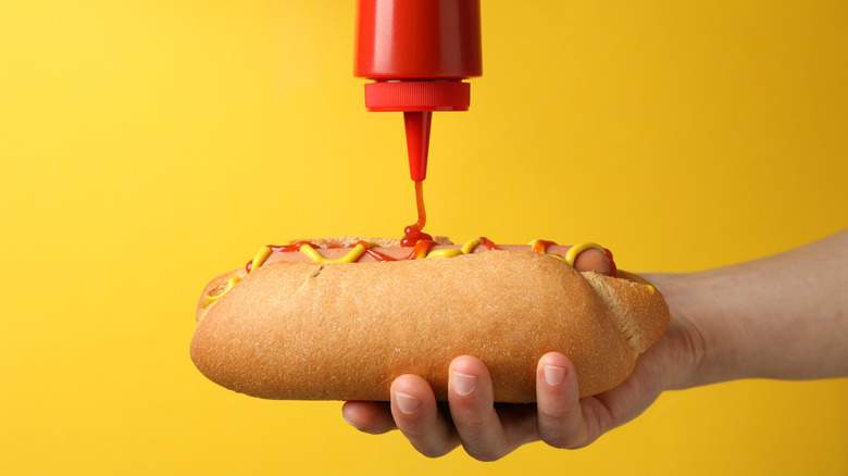 Someone pours ketchup on a hot dog