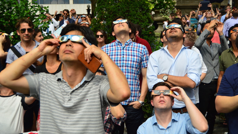 A crowd of people watch the solar eclipse using special glasses to protect their eyes from damage