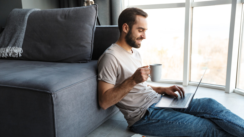 a man at home, drinking tea with laptop