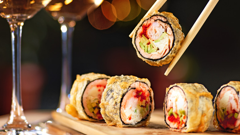 Someone holds a sushi roll with chopsticks