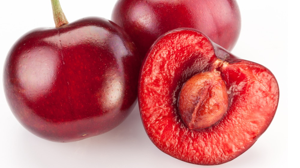 Two whole cherries on the stem and a third cherry cut in half to reveal the pit