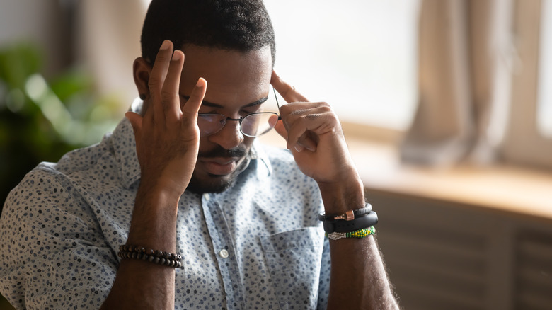 Man sitting with eyes closed and fingers at his temples